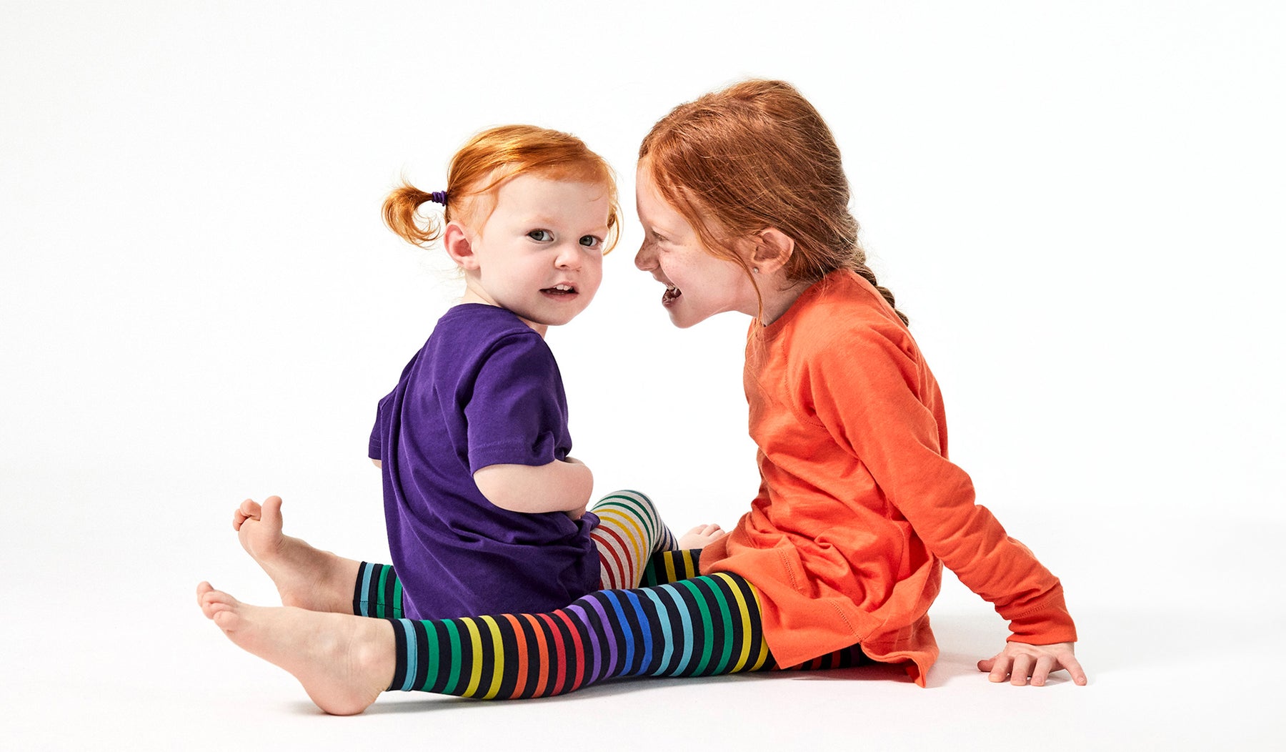 two little girls wearing tunics and striped rainbow leggings talking to each other